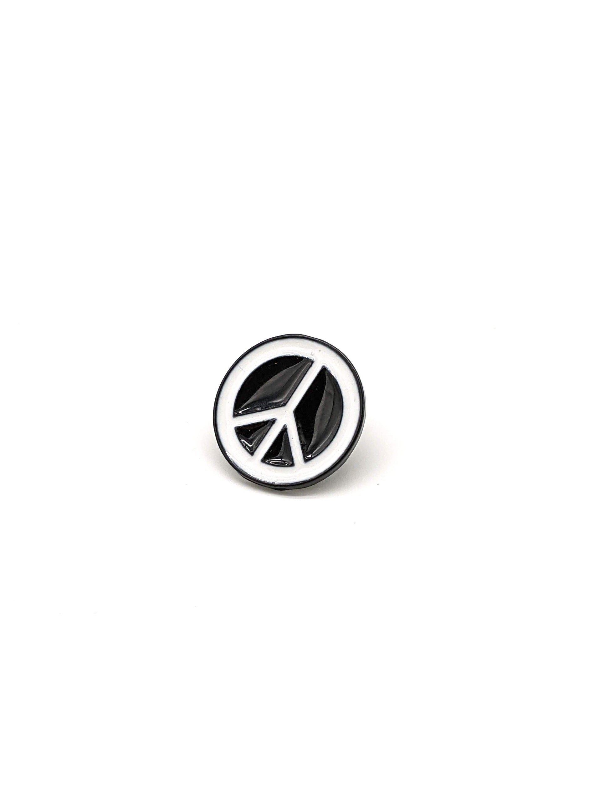 A black and white peace symbol brooch designed to be attached to a hat.