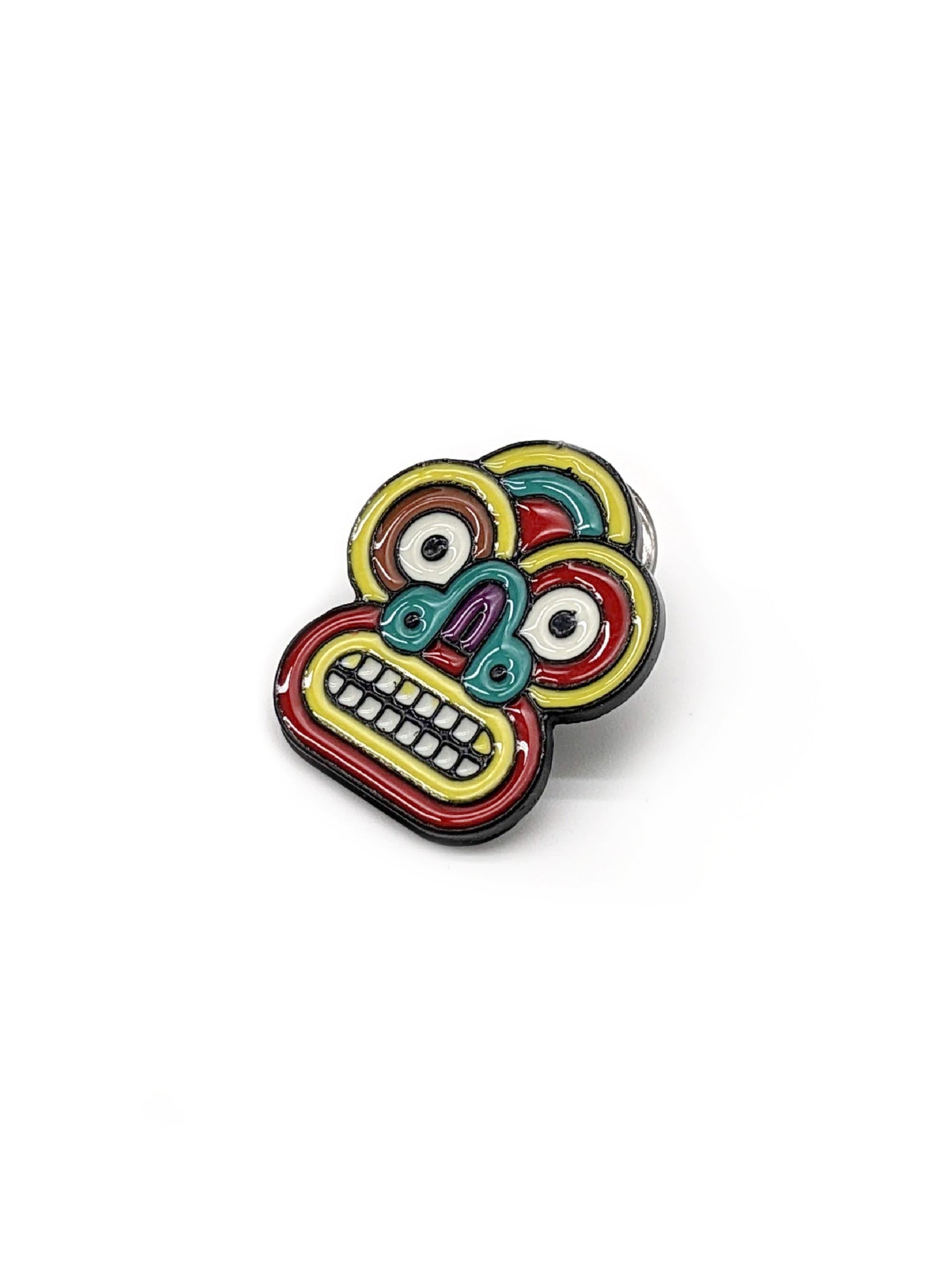 A colorful brooch in the shape of a tribal mask designed to be attached to a hat.